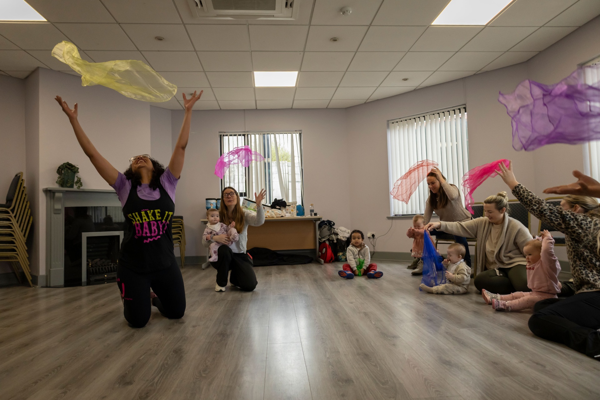 Jessica throwing colourful scarves with mums and babies during a Zumbini class